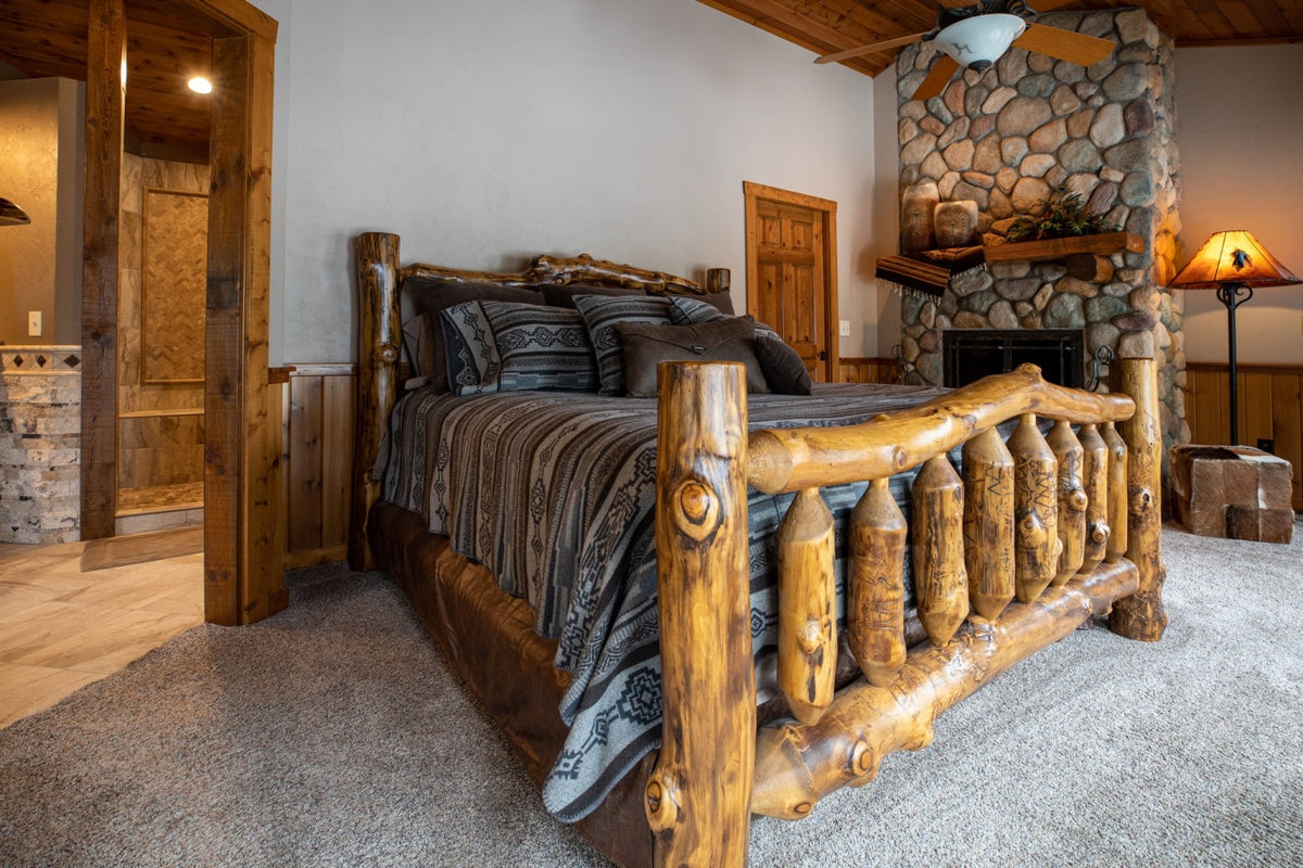 Log bed with a tall headboard beside a stone fireplace, Antler Lake Lodge project, Northern Wisconsin