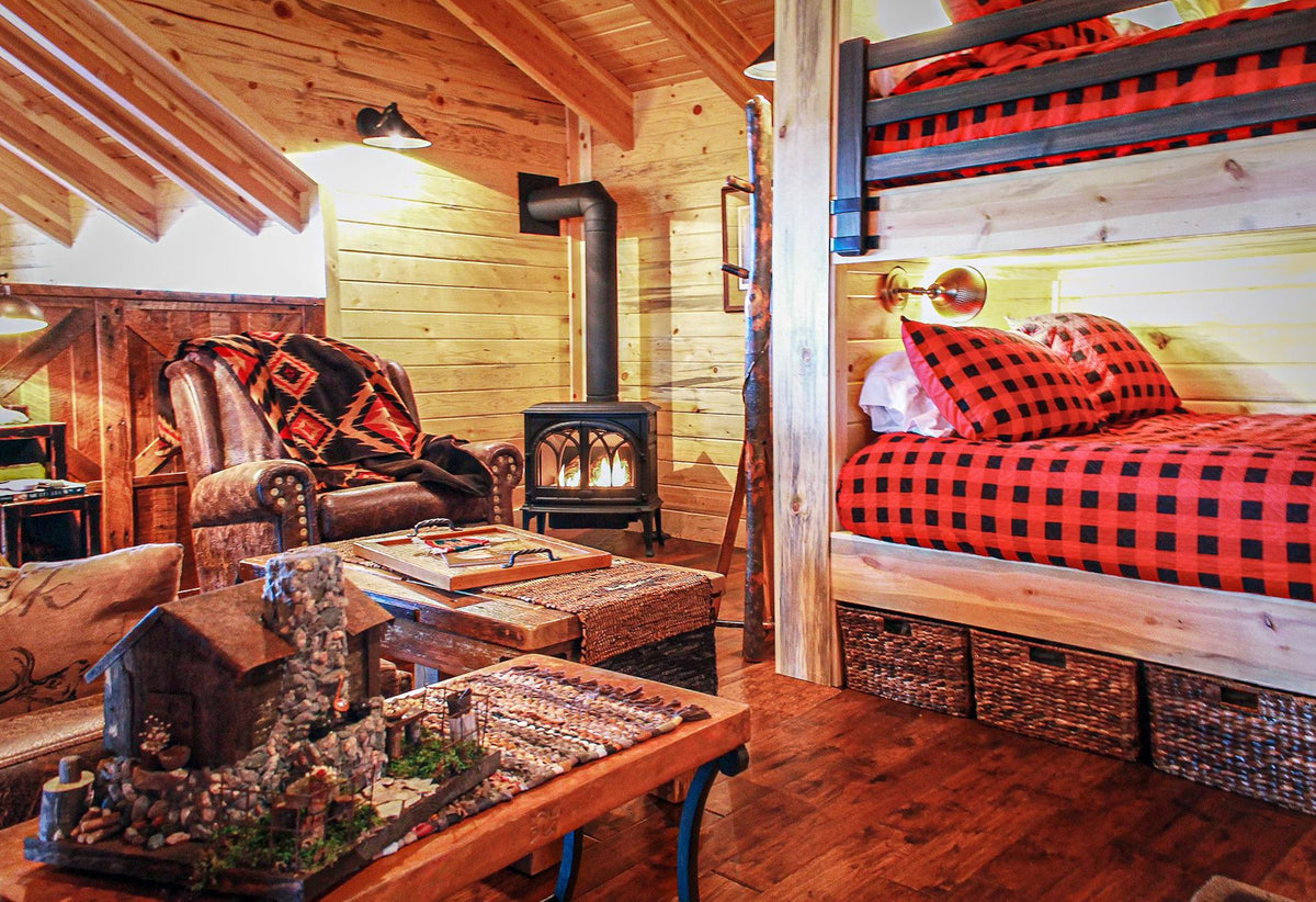Bunk room with red buffalo-check bedding, a wood stove and a leather armchair, Beresford Lodge project, Eastern Wisconsin