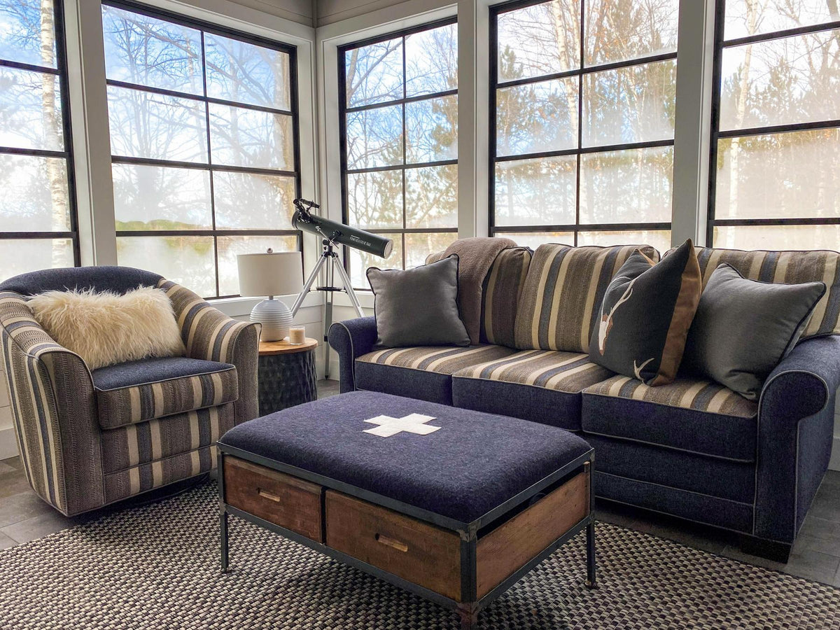 Sunroom with a navy striped sofa and a wall of windows facing the woods, Dreamer's Lake project, Central Wisconsin