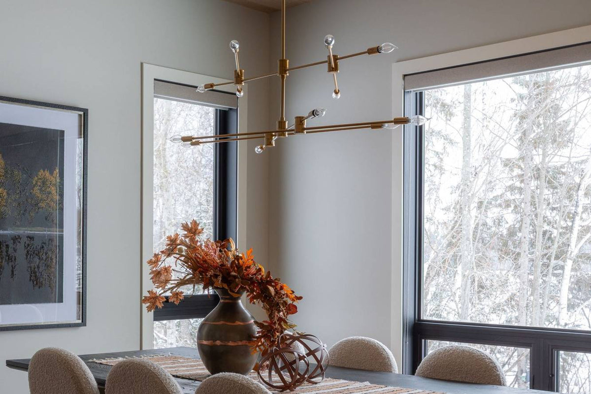 Dining room with a brass linear chandelier, a dark table, boucle chairs and black-framed windows, Black Diamond project