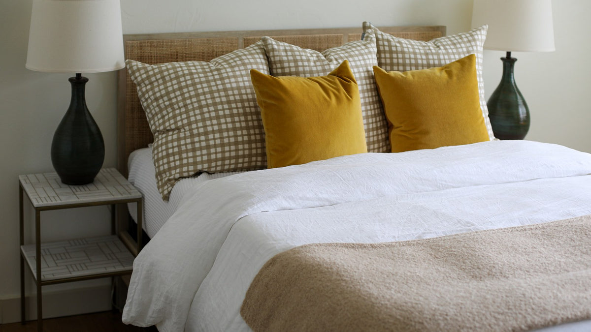 Bed with crisp white bedding, plaid and mustard pillows and matching black lamps